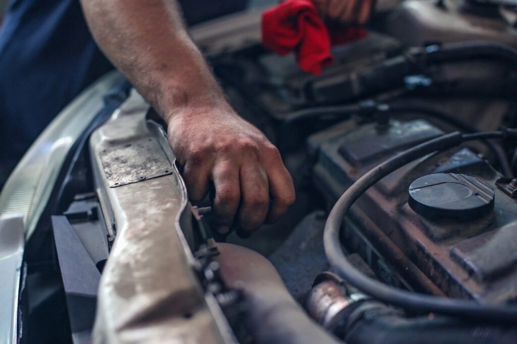 Mechanic repairing a car engine in a garage, using tools to inspect and fix vehicle components